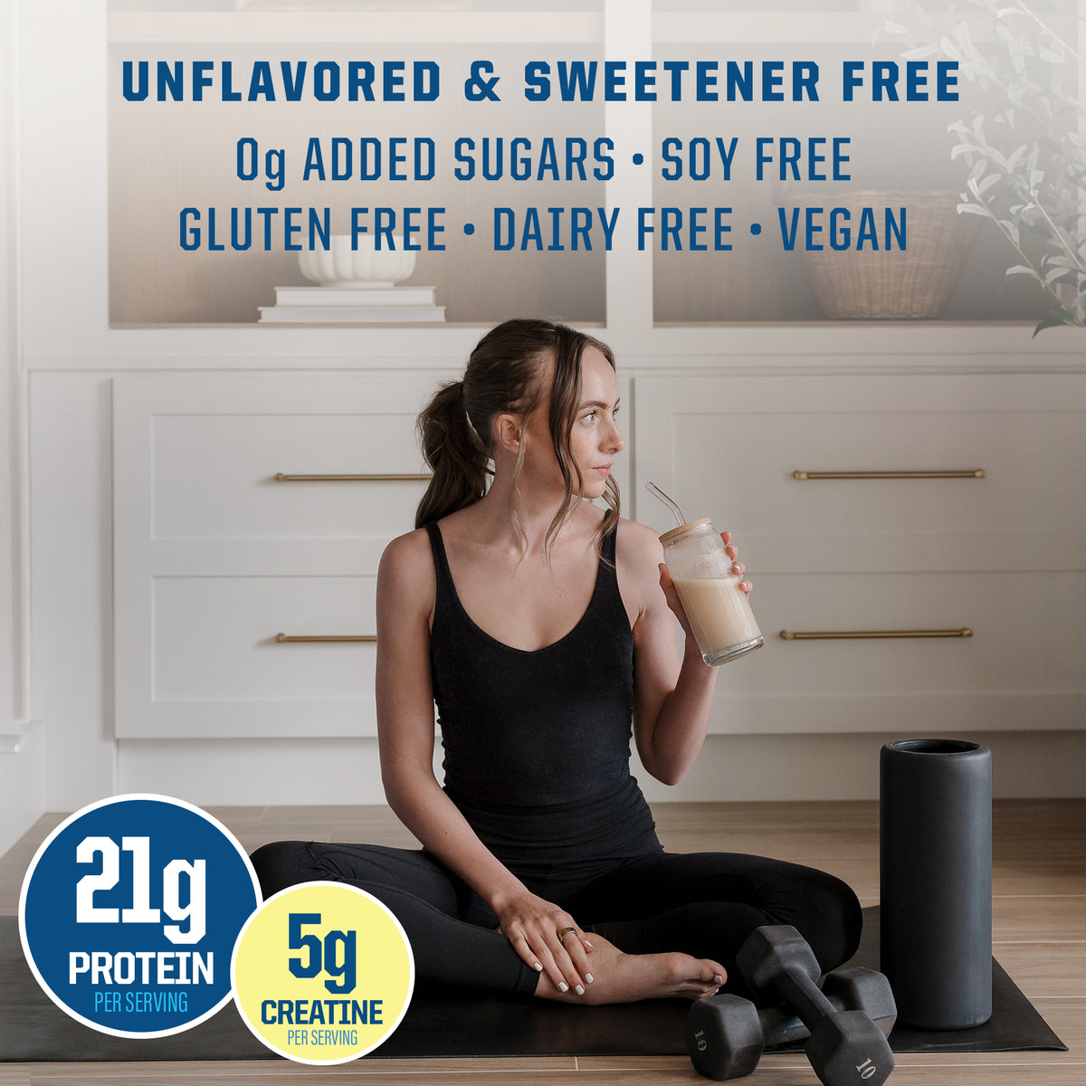 Woman in black workout clothes sitting on a mat holding a protein shake beside dumbbells and foam roller.