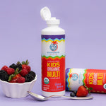 Bottle of organic kids’ multivitamin with omega, surrounded by fresh berries and a spoon on purple background