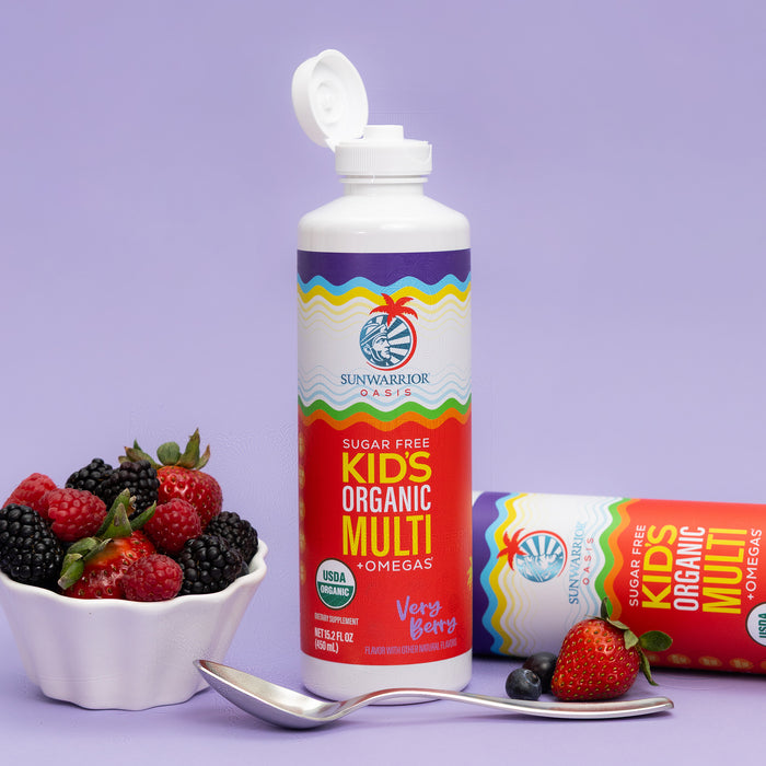 Bottle of organic kids’ multivitamin with omega, surrounded by fresh berries and a spoon on purple background