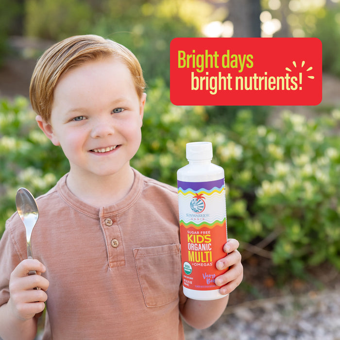 Young boy outdoors holding a spoon and a bottle of organic kids multivitamin with bright nutrients text